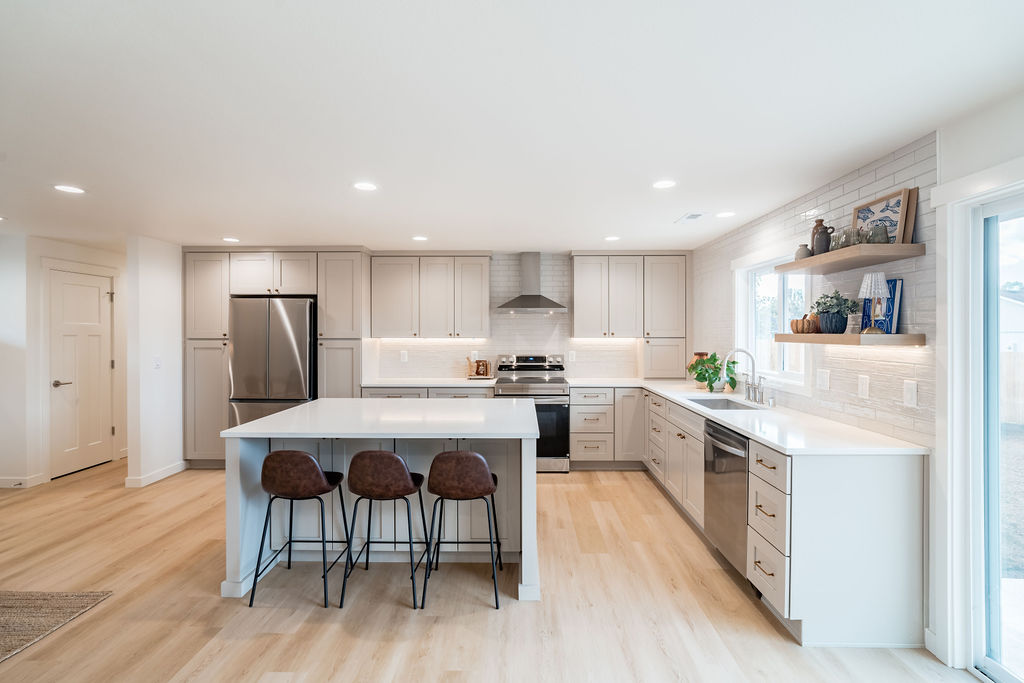 Bright open kitchen with island, gray shaker cabinets, quartz counters, and stainless appliances after renovation
