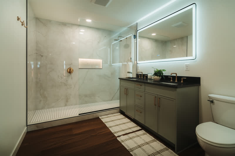 Remodeled bathroom with marble walk-in shower, brass fixtures, and backlit mirror